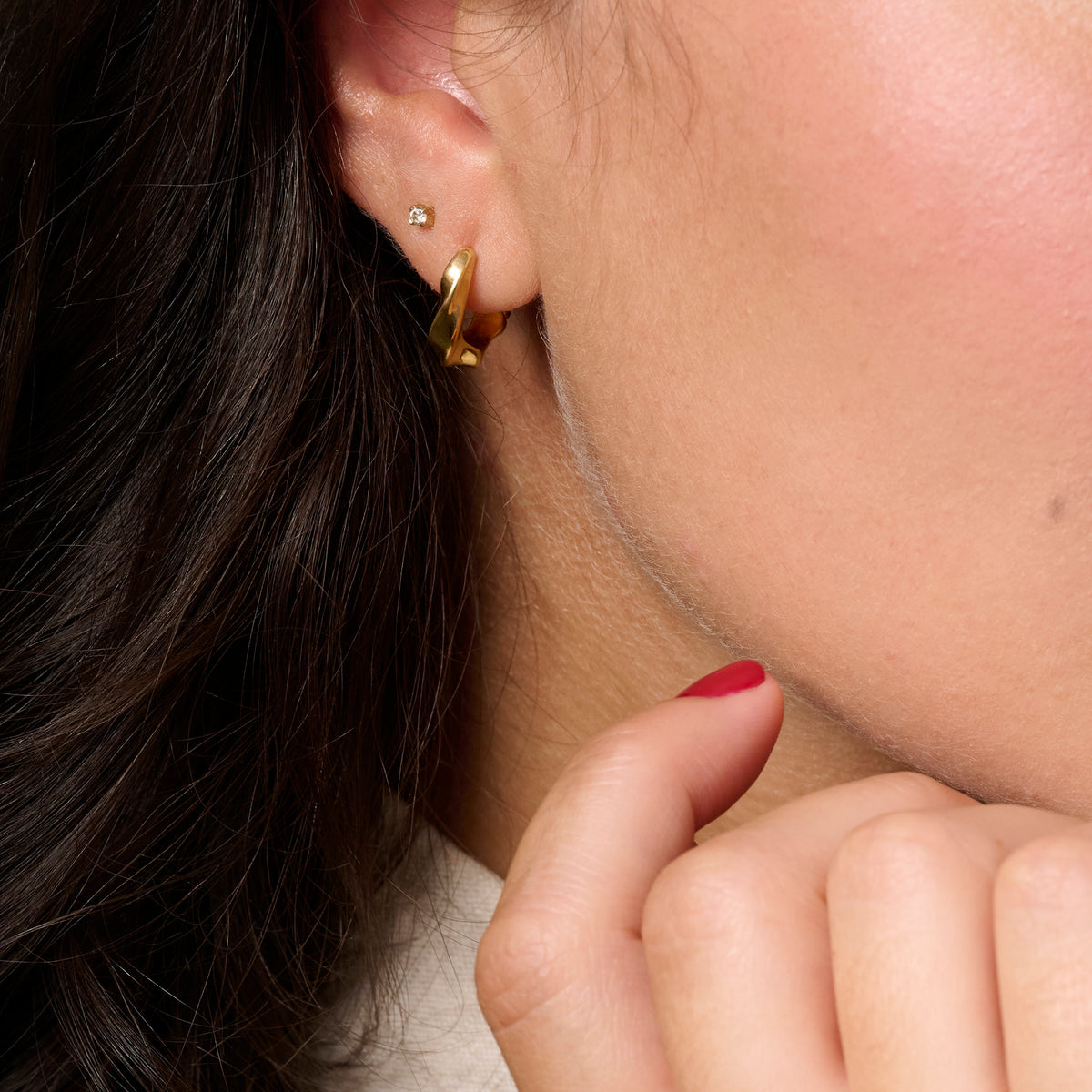 Close-up of a person's ear wearing a gold huggie twisted hoop earring and a small diamond stud earring.
Gros plan sur l'oreille d'une personne portant une boucle d'oreille anneau dorée torsadée et un petit clou serti d'une pierre.
