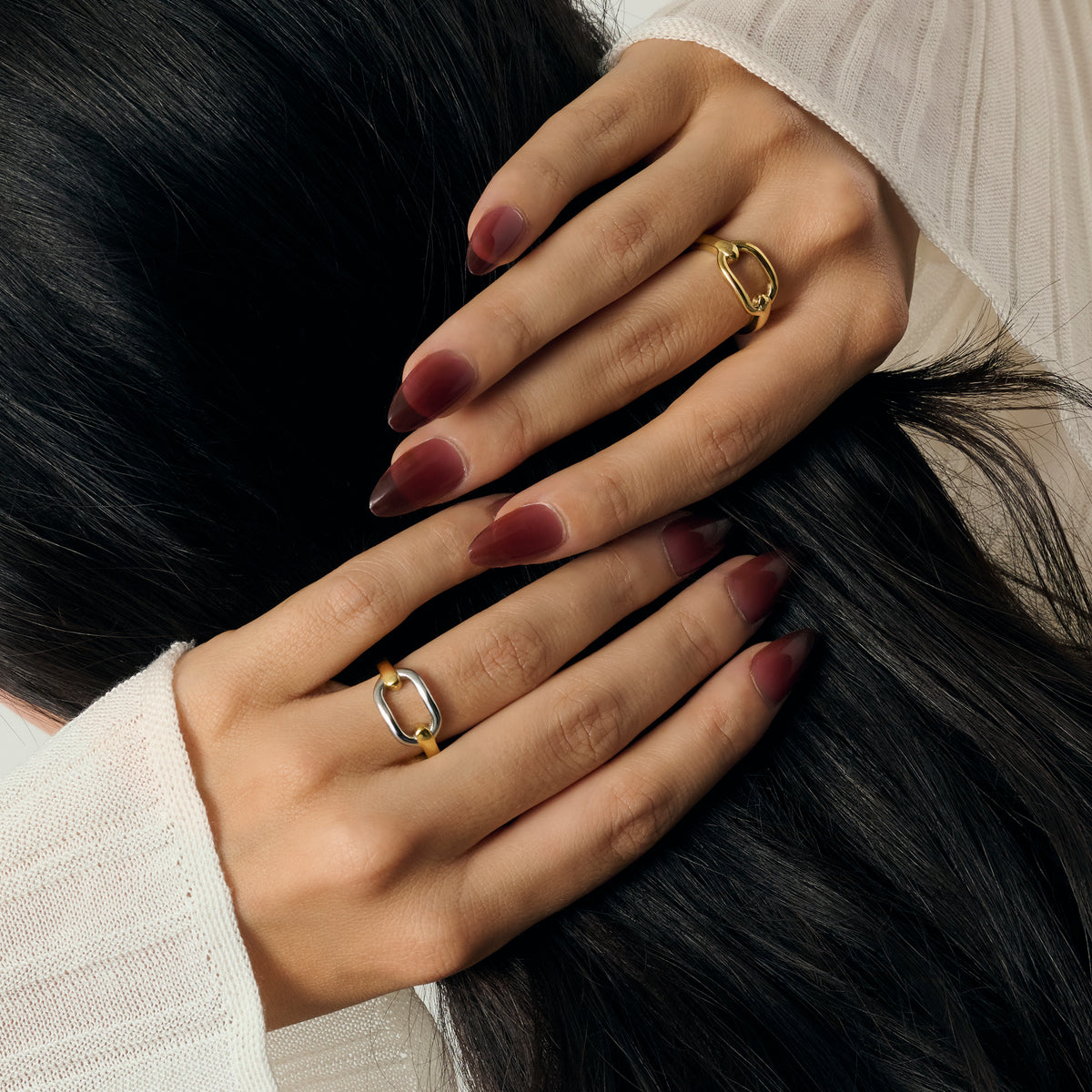 Close-up lifestyle shot of a woman's hands wearing a gold oval-motif ring and a two-tone gold and silver oval-motif ring, styled with a cream knit sweater. Nickel-free jewelry.
Photo lifestyle en gros plan des mains d'une femme portant une bague dorée à motif ovale et une bague bicolore dorée et argentée à motif ovale, agencées avec un tricot crème. Bijoux en acier inoxydable sans nickel.